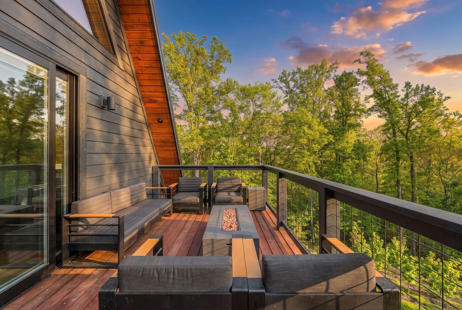 An open deck with a fire table on an A-frame cabin, looking over the treetops near Asheville at sunset